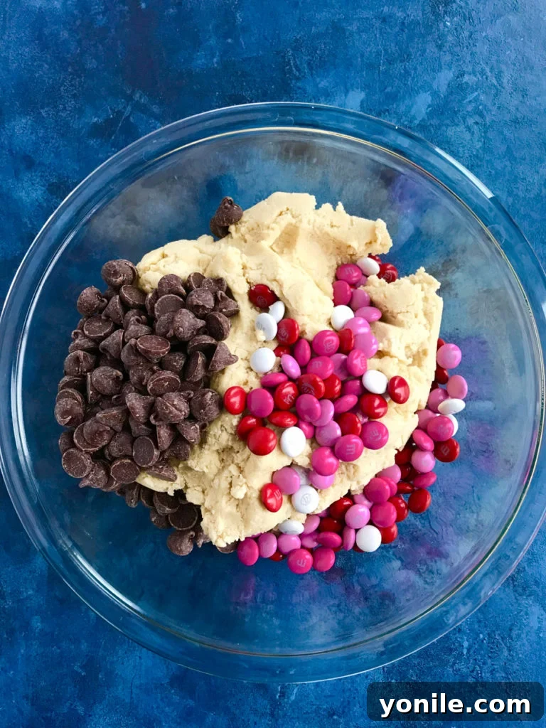 Hands mixing cookie dough in a bowl for Valentine's M&M Chocolate Chip Cookie Bars.