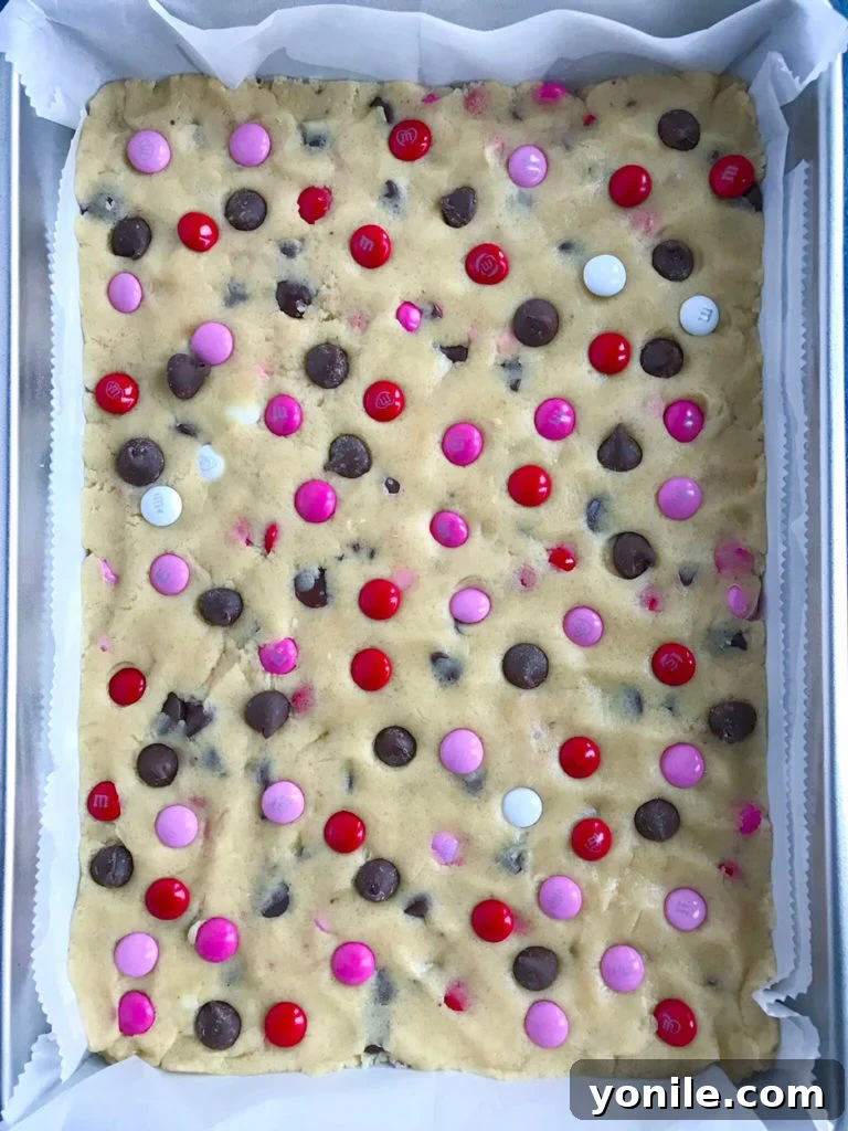 Close-up of cookie dough with M&M's and chocolate chips being gently mixed.