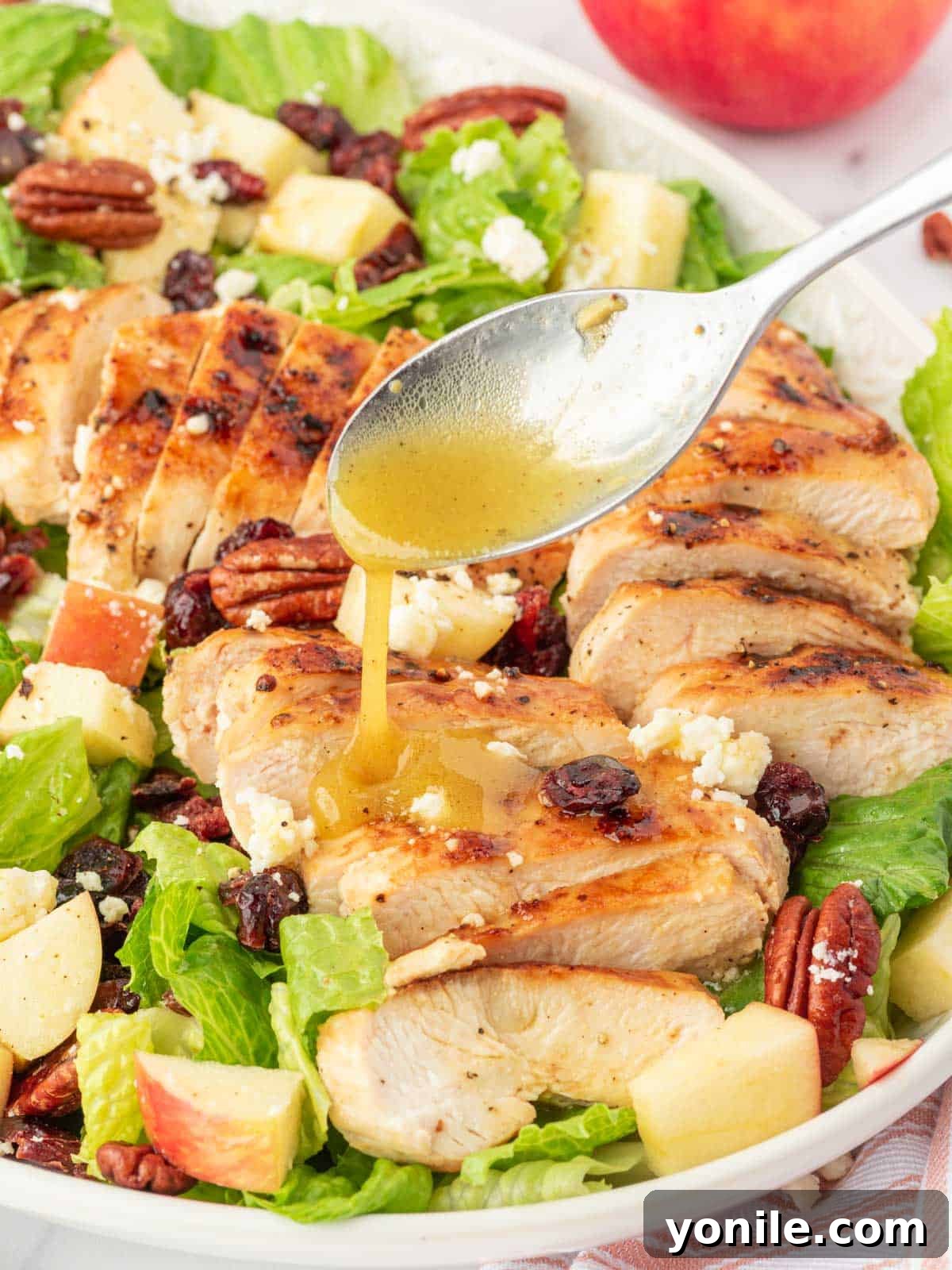 Autumn Harvest Chopped Chicken Salad 8 A spoon drizzles maple dressing over the autumn chopped salad on a serving platter.