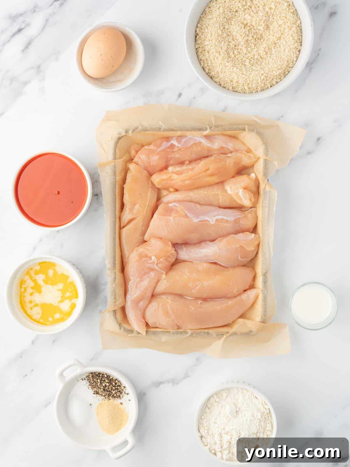 Oven-Crisped Buffalo Tenders 3 Assortment of fresh ingredients needed for baked buffalo chicken tenders, including chicken, flour, seasonings, and hot sauce.