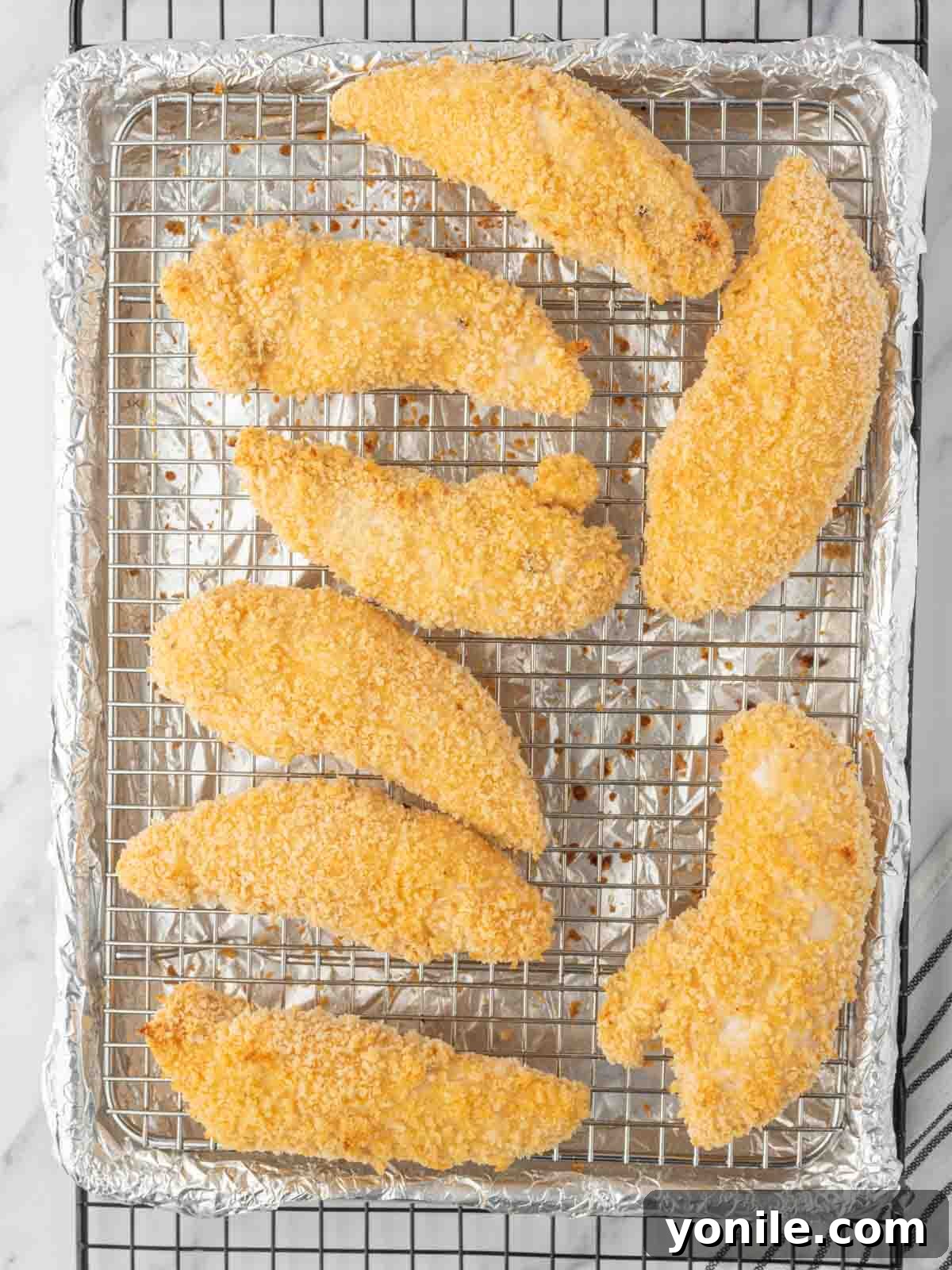 Oven-Crisped Buffalo Tenders 5 Crispy breaded chicken tenders arranged on a wire rack for baking.