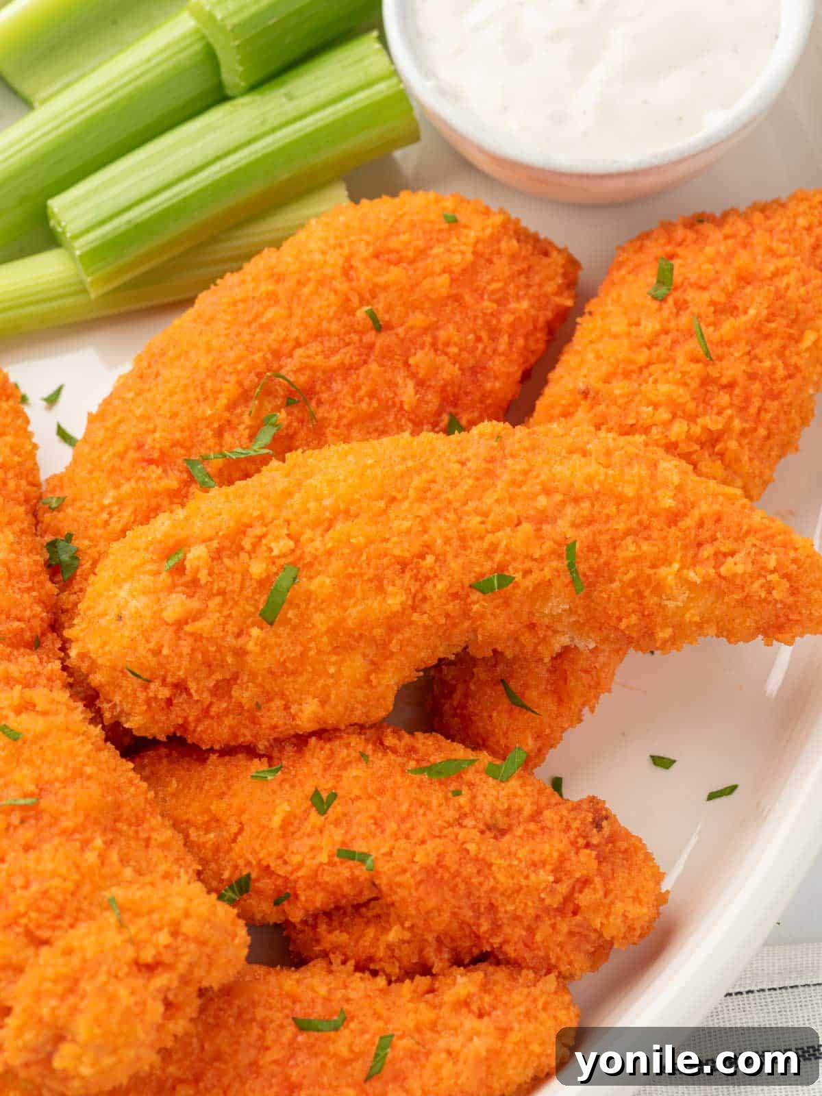 Oven-Crisped Buffalo Tenders 7 A vibrant plate of buffalo chicken tenders served with a side of dipping sauce and fresh celery.