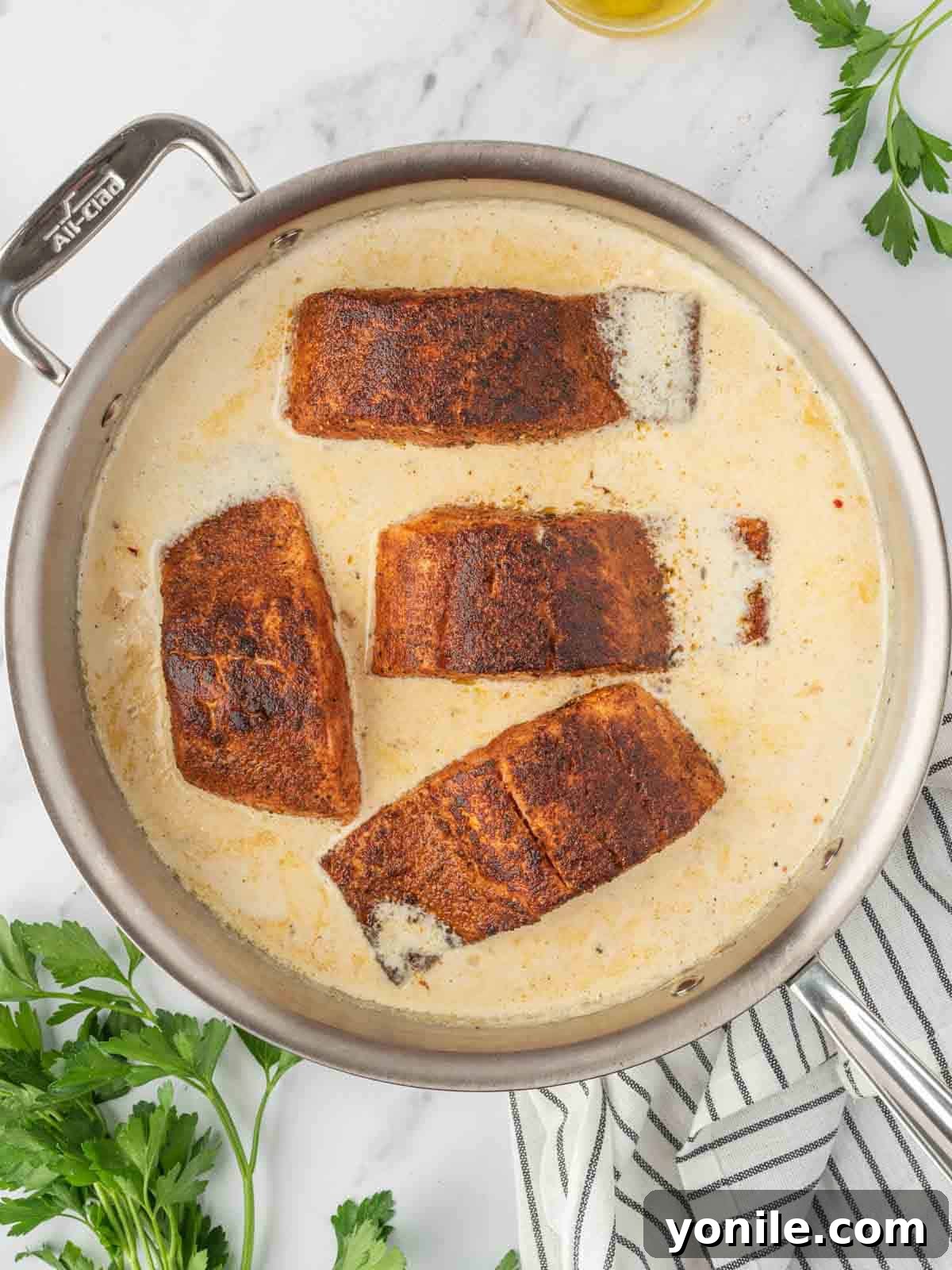 Blackened salmon in a skillet with creamy sauce, simmering.