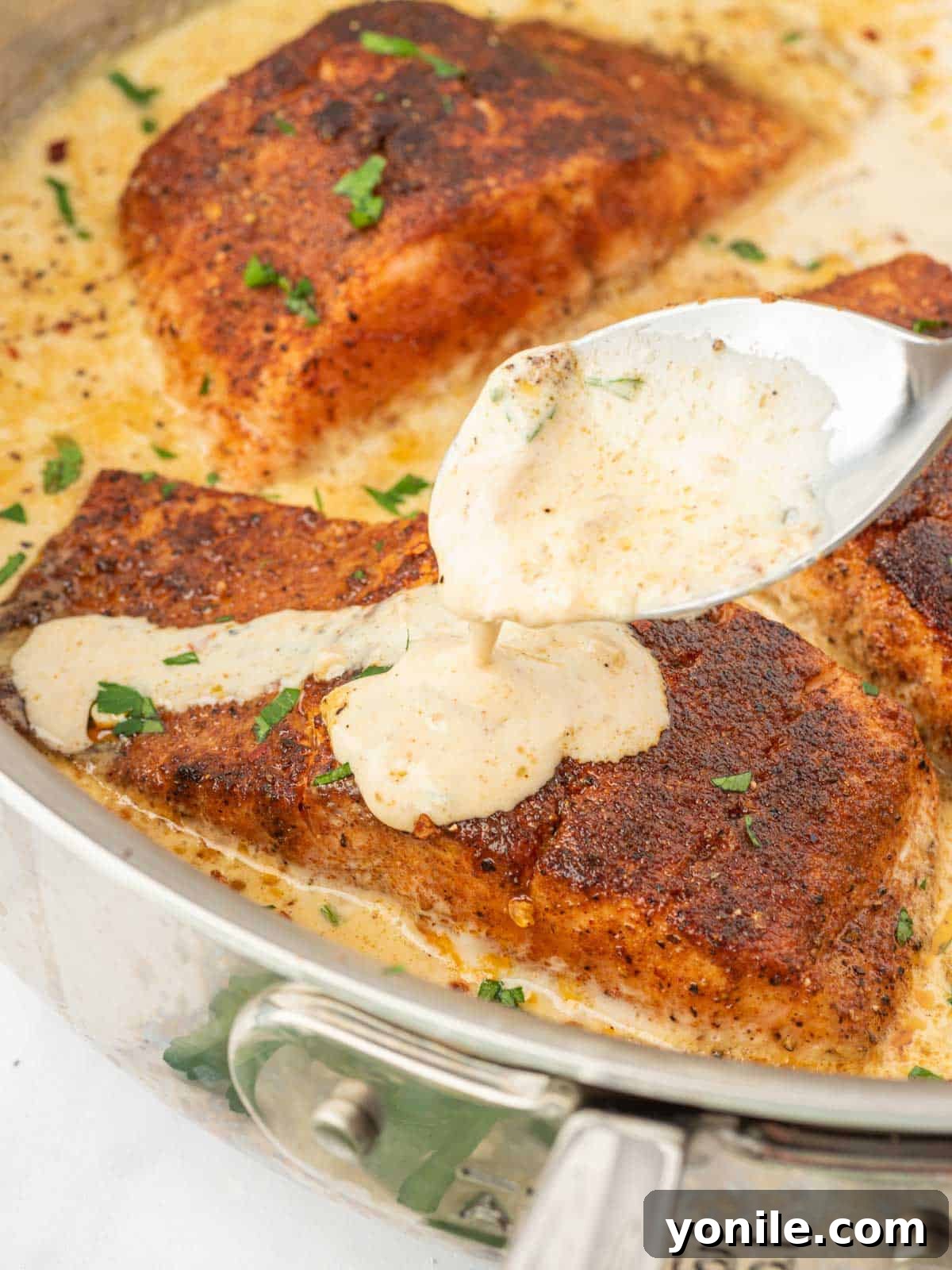 Cajun salmon with a spoon drizzling cream sauce over it.