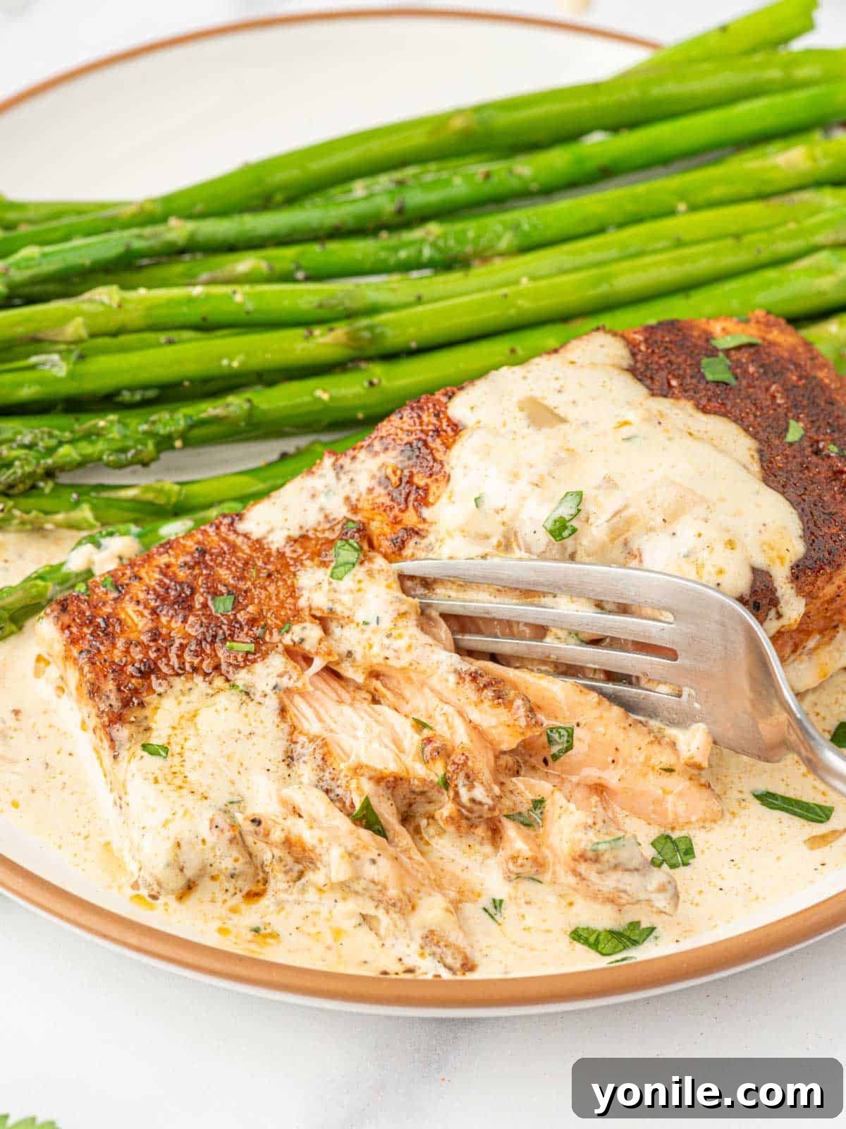 Flaking salmon with a fork on a plate with asparagus.