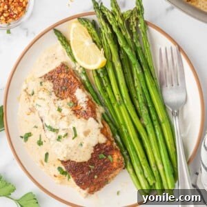 A plate with asparagus spears and a piece of salmon with cream sauce and a fork.