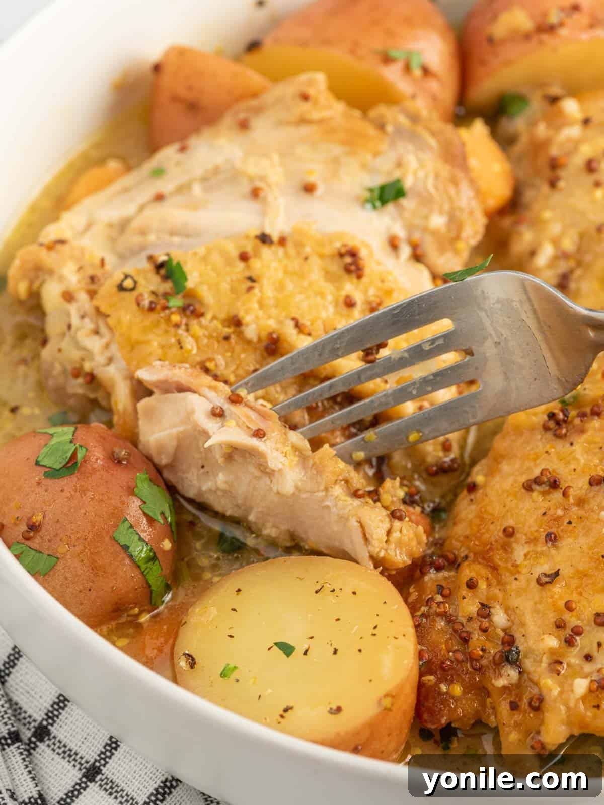 A fork picking up a succulent piece of honey Dijon chicken thigh from the Instant Pot stew, showcasing its tenderness.