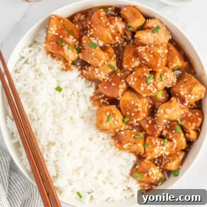 Chinese sesame chicken in a bowl with rice and chopsticks resting on the side.