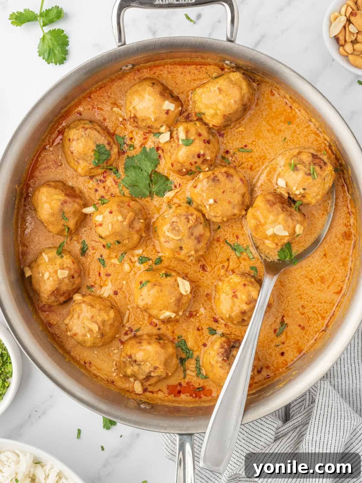 Succulent Thai chicken meatballs simmering in a creamy coconut curry sauce in a cast-iron skillet, garnished with fresh cilantro.