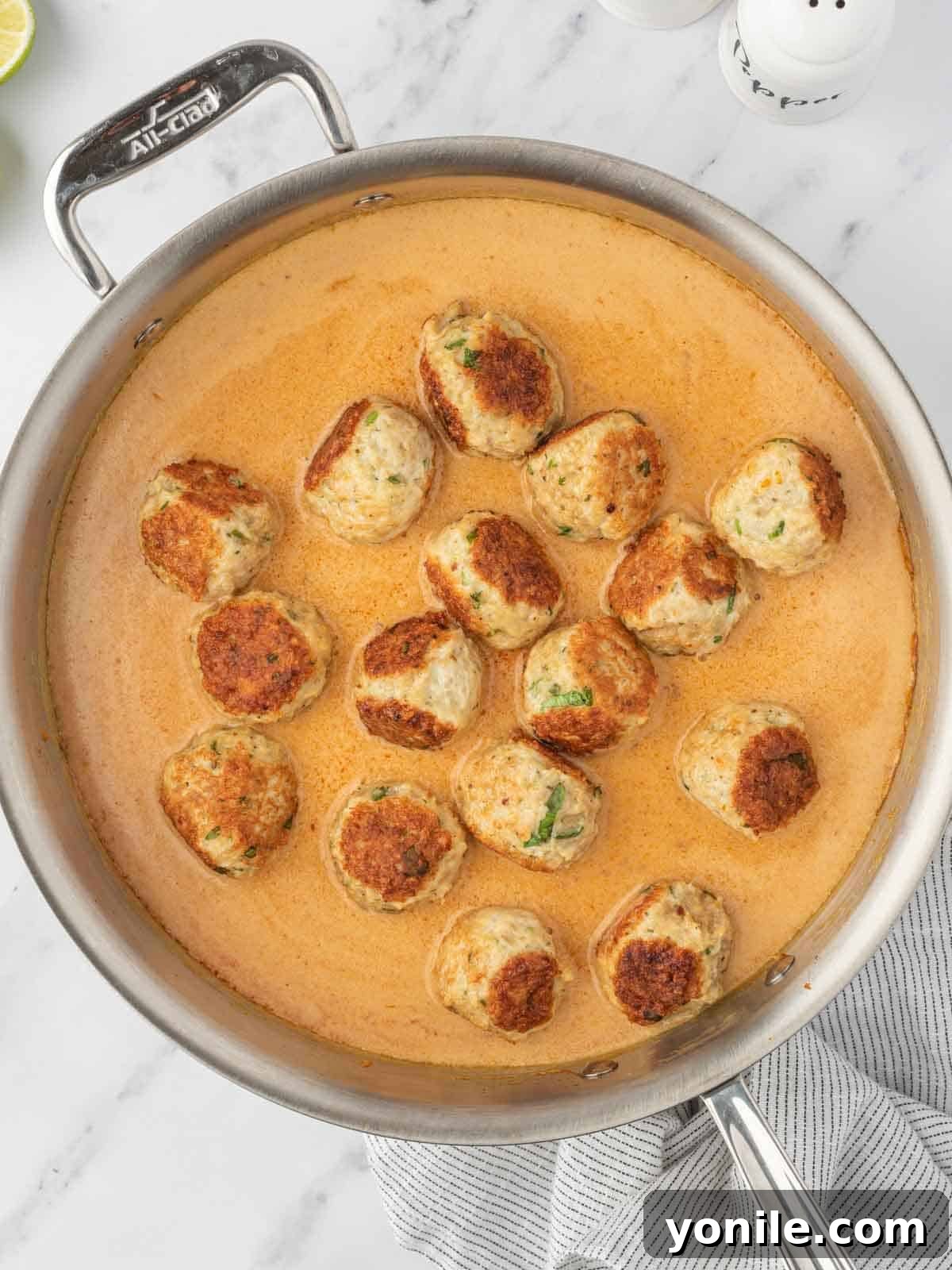 Cooked chicken meatballs being added back into the rich coconut curry sauce in a skillet.