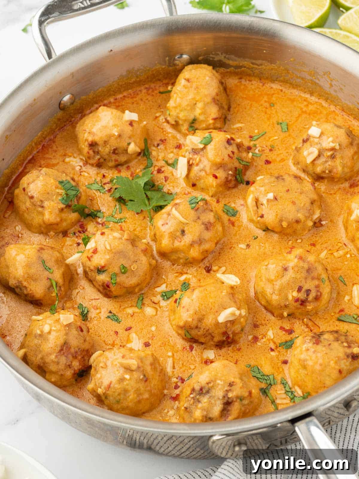 A vibrant close-up of Thai chicken meatballs in a skillet, bathed in a rich curry sauce and topped with fresh herbs.