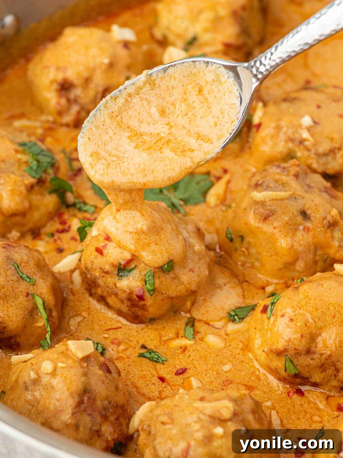 A spoon delicately drizzles rich coconut curry sauce over tender Thai chicken meatballs, highlighting the creamy texture.