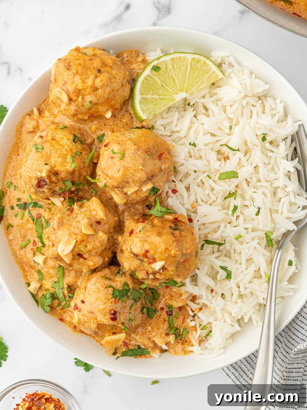 A white bowl filled with Thai chicken meatballs and fluffy rice, garnished with cilantro and a fork ready to enjoy.