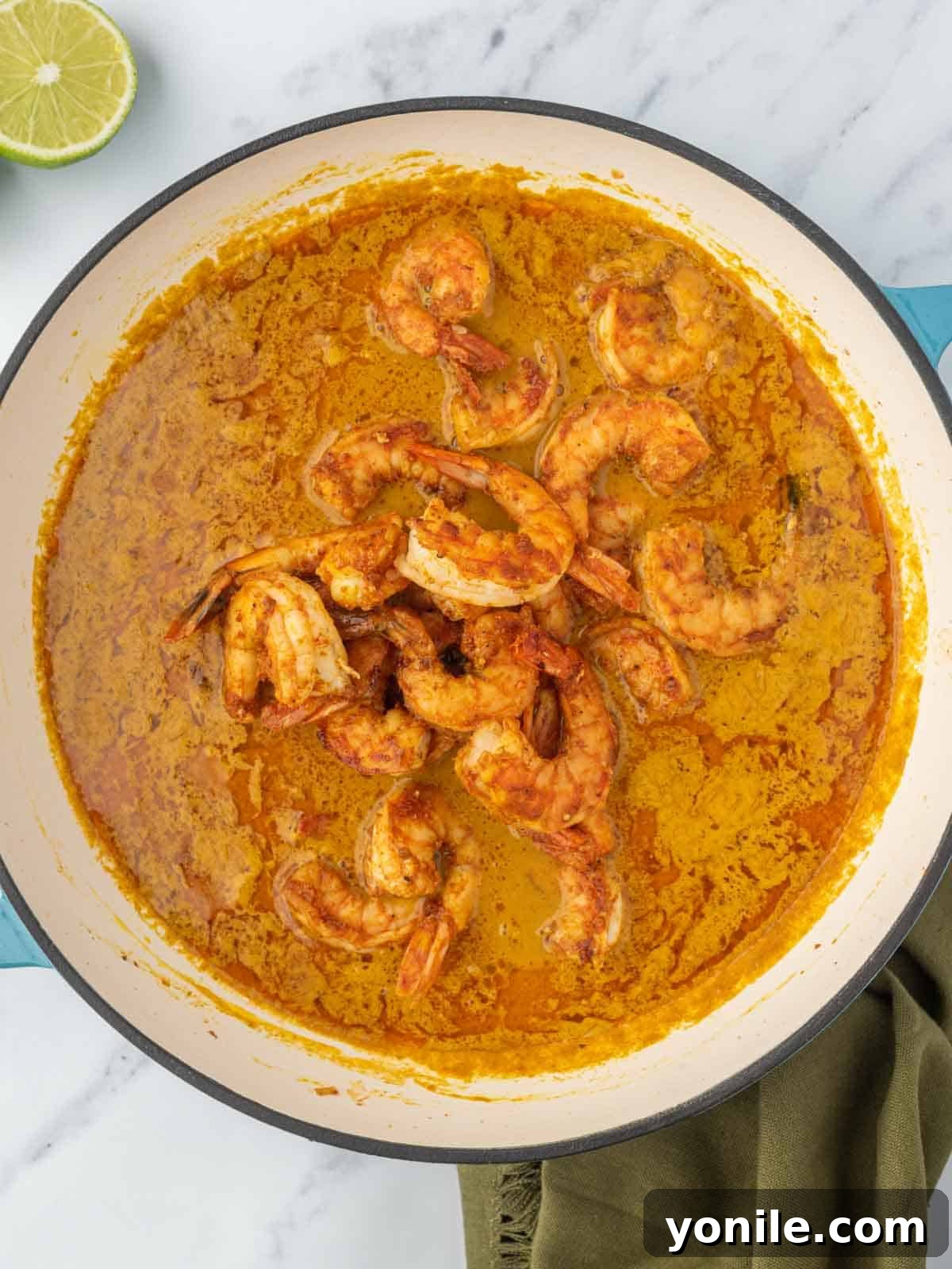 Vibrant Thai Coconut Shrimp Curry 6 Shrimp being gently added to a simmering pot of rich red curry sauce in a skillet.