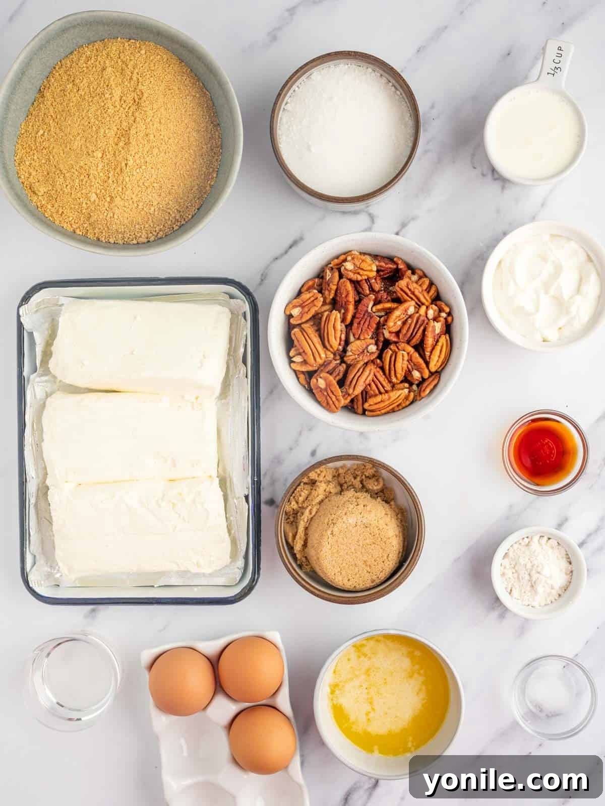 Fresh ingredients laid out for making a delicious pecan pie cheesecake, including graham crackers, cream cheese, pecans, and butter.