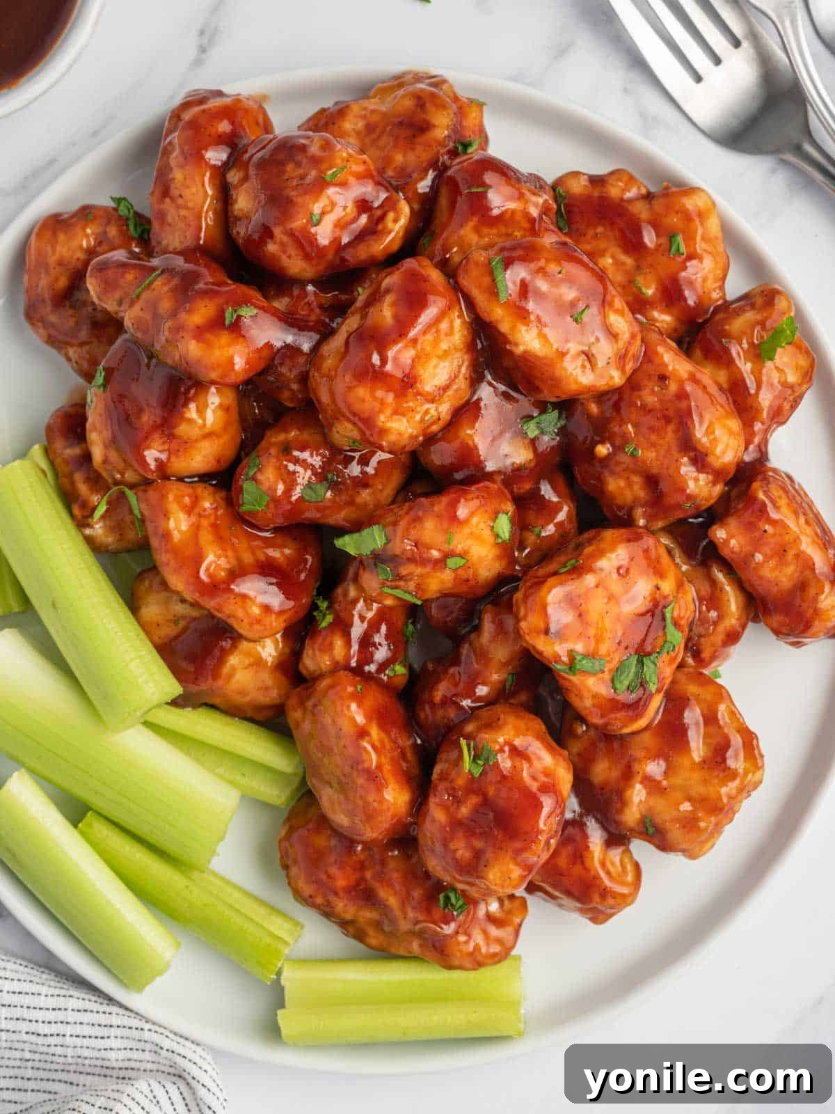 Top view of baked BBQ chicken bites with celery sticks arranged on a white plate, showcasing their sticky, glossy sauce.