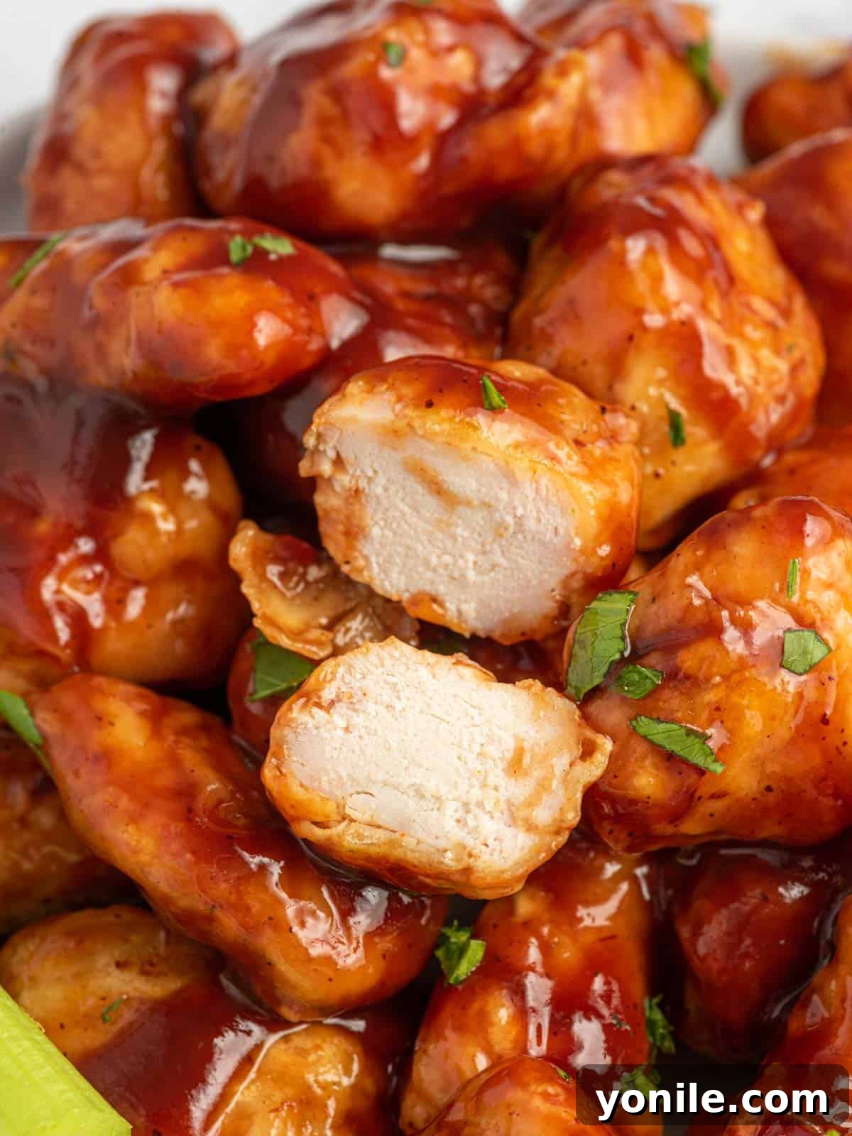 A baked BBQ chicken bite expertly cut in half to reveal its tender, juicy interior, resting on a pile of other glazed chicken pieces.