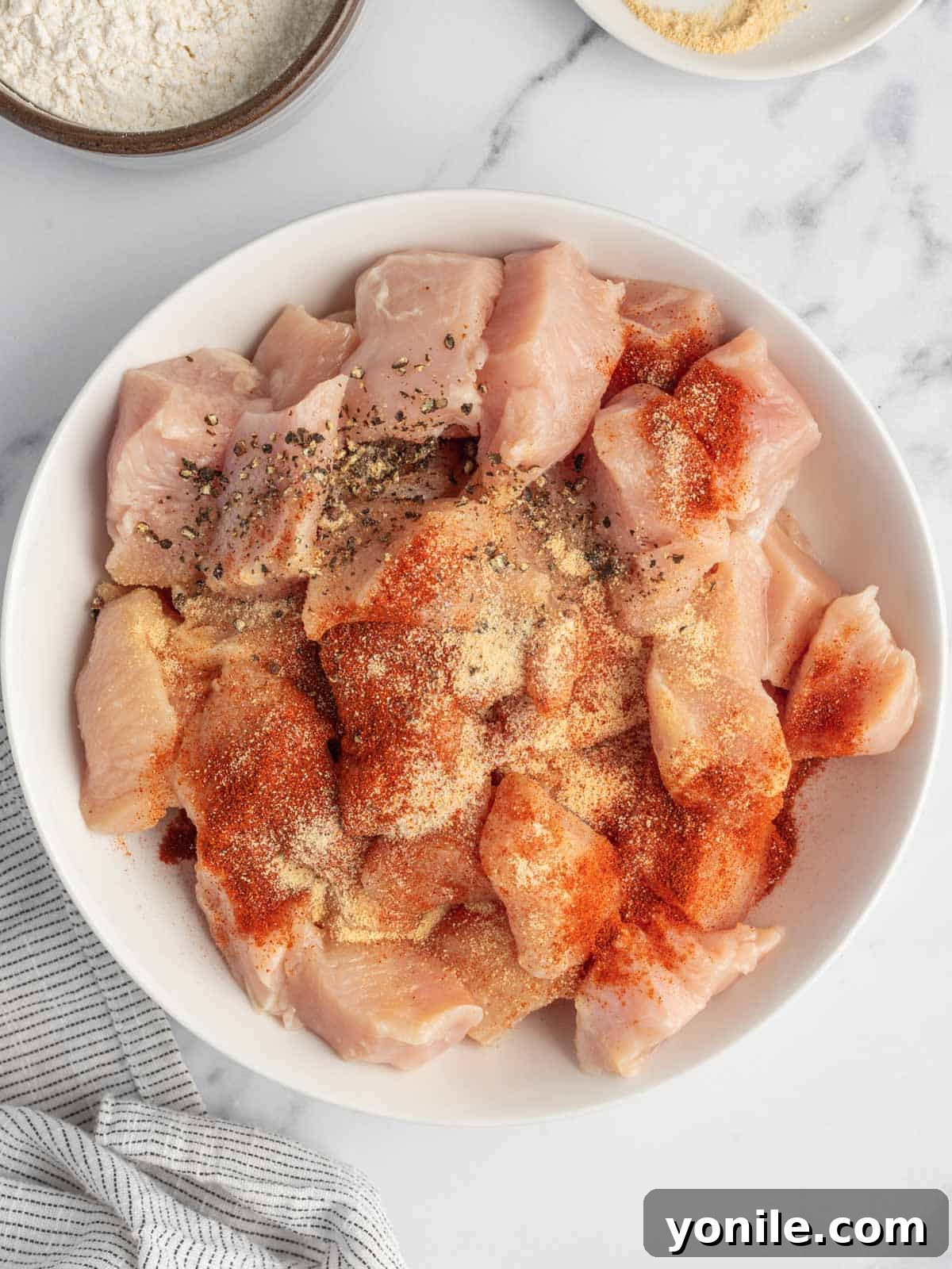 Chicken pieces being tossed with seasoning in a bowl, showing the paprika, garlic powder, salt, and pepper coating.