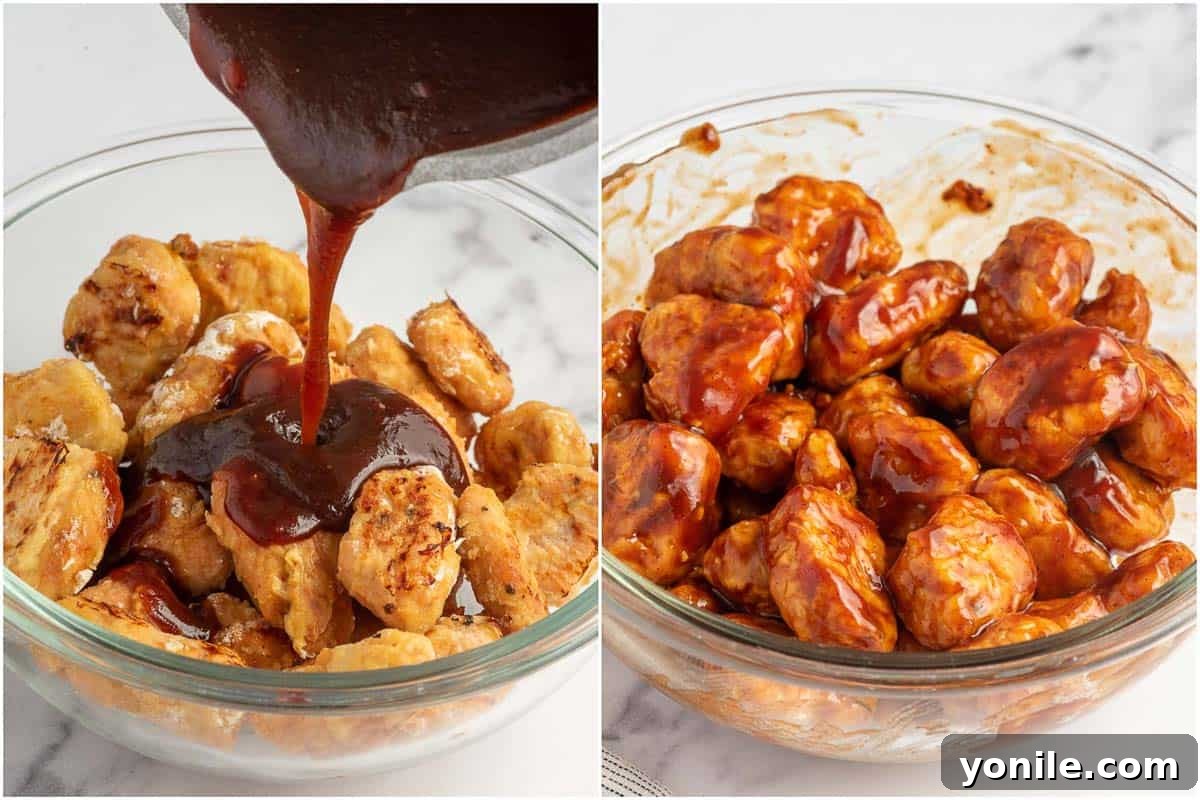 Baked chicken bites being generously coated with rich BBQ sauce in a large mixing bowl.