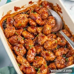 A spoon scoops baked honey sesame chicken breast from a casserole dish.