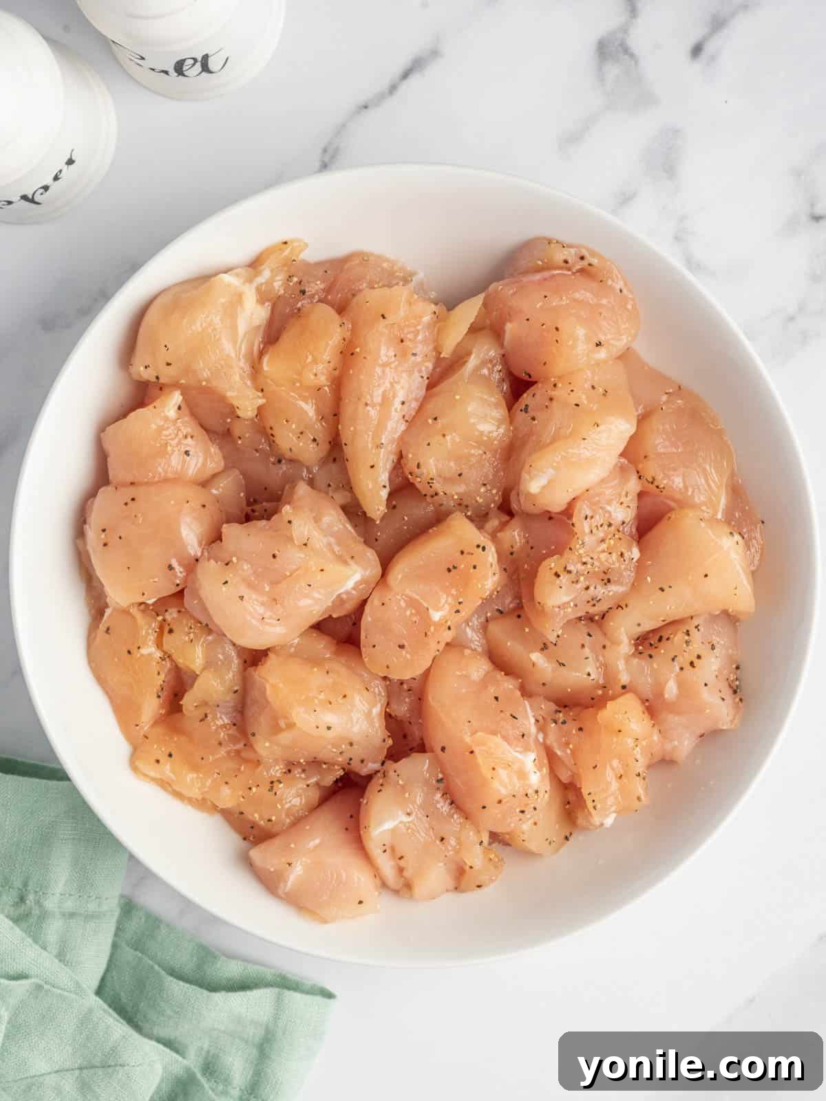 Chicken breast seasoned with salt and pepper in a white bowl.