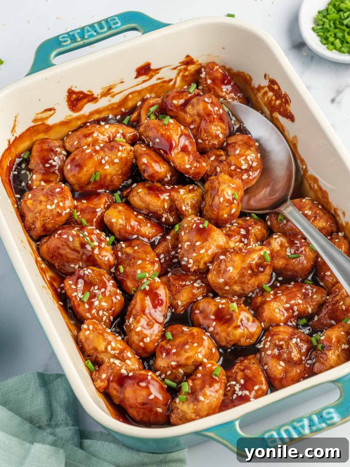 A spoon scoops baked honey sesame chicken breast from a casserole dish.