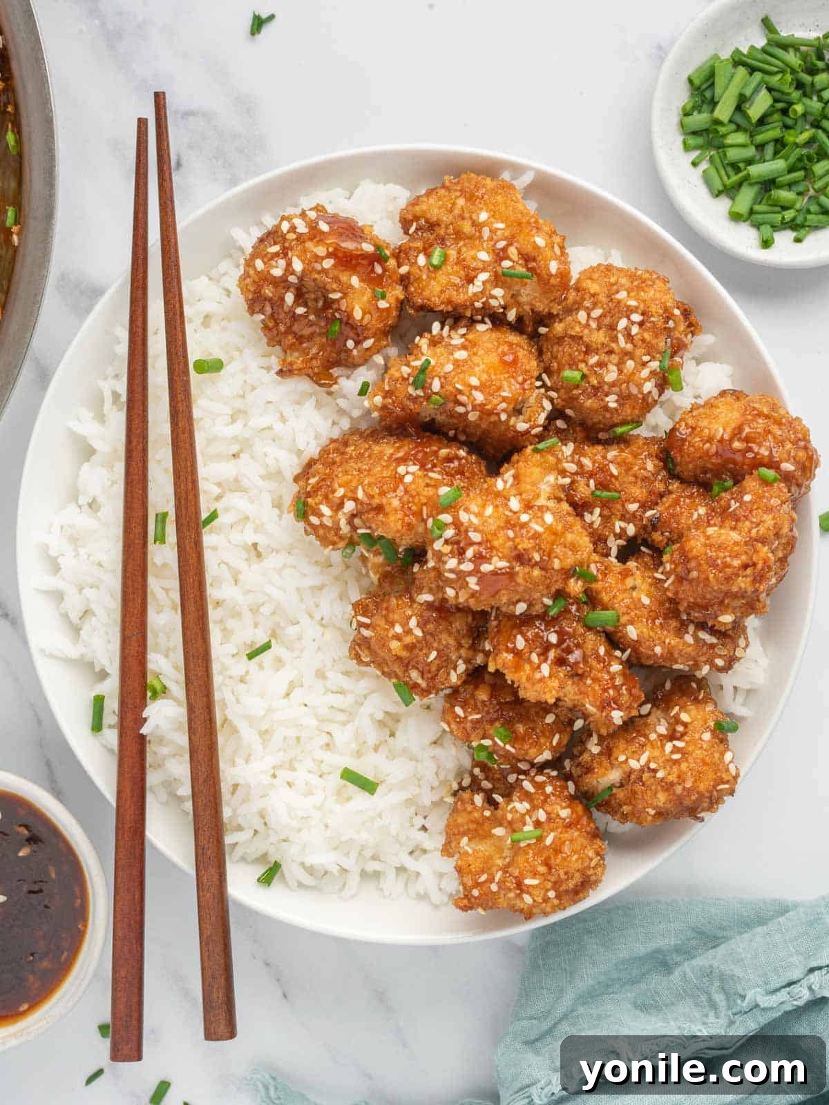 Chop sticks rest on a bowl of rice and vegan sesame cauliflower.