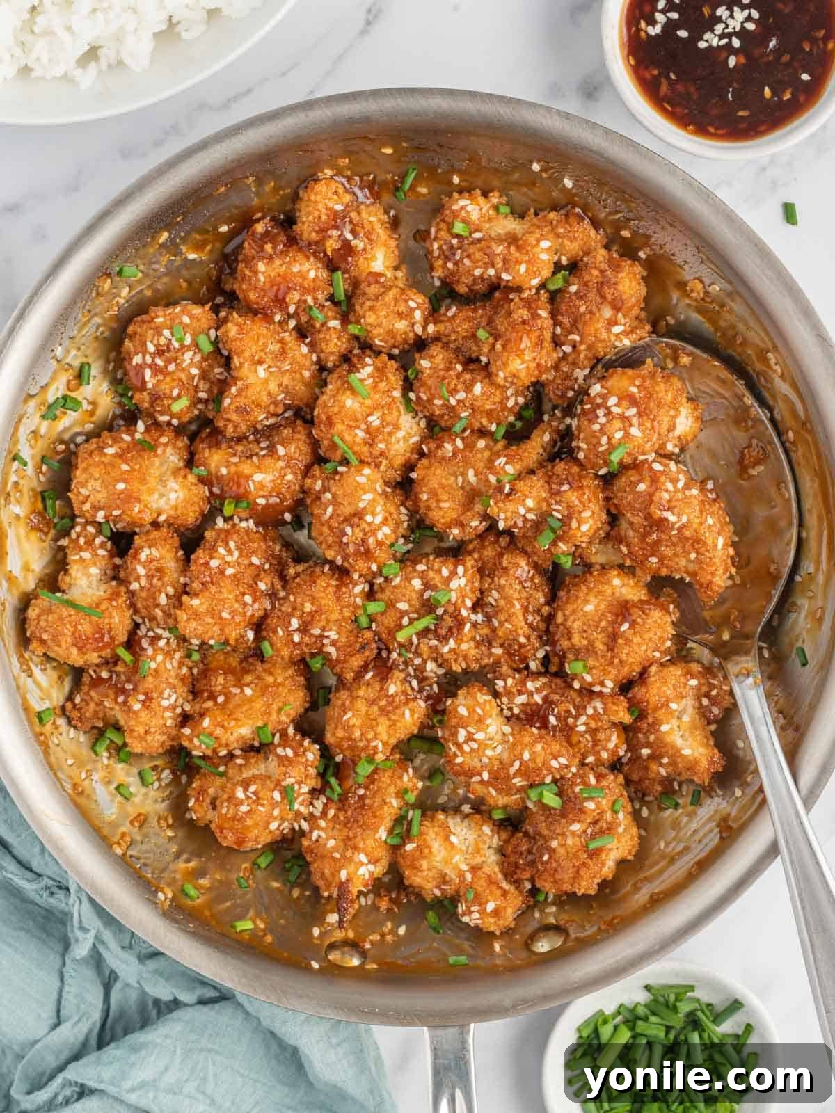 A pan of stick sesame cauliflower bites with a spoon and bowls of garnish.