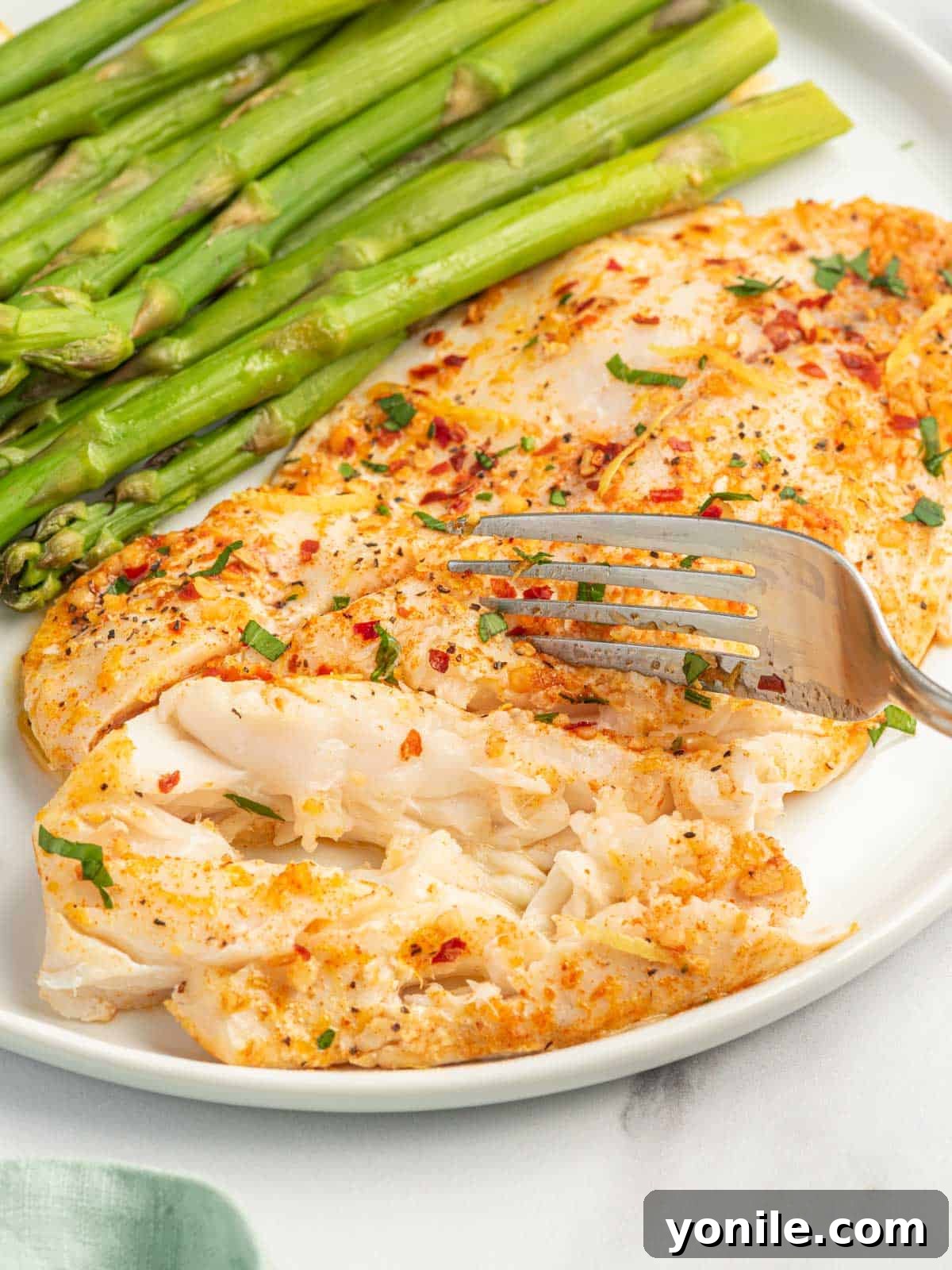A fork flakes a garlic butter tilapia filet on a plate.