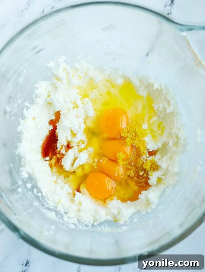 Close-up of wet ingredients for pear cake, including butter, sugar, eggs, and vanilla, in a mixing bowl.
