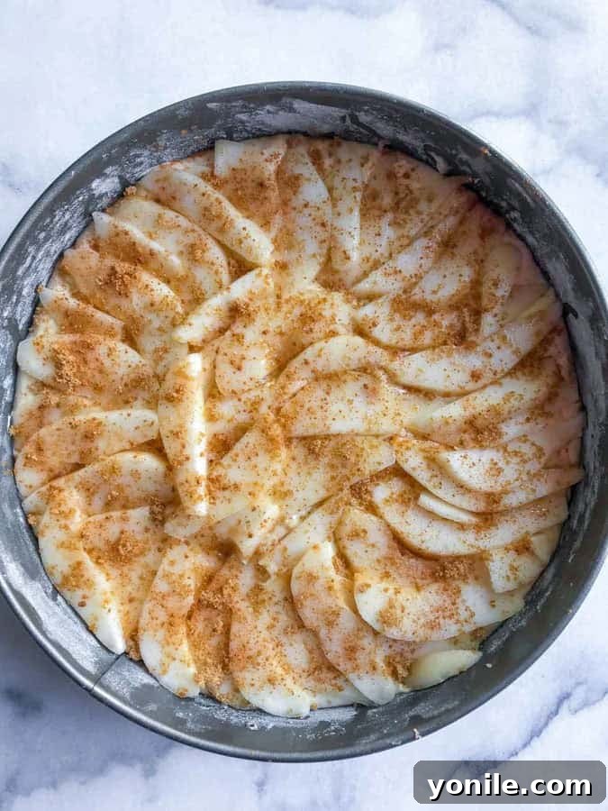 Moist pear cake batter topped with sliced pears, cinnamon, and brown sugar, ready for the oven.