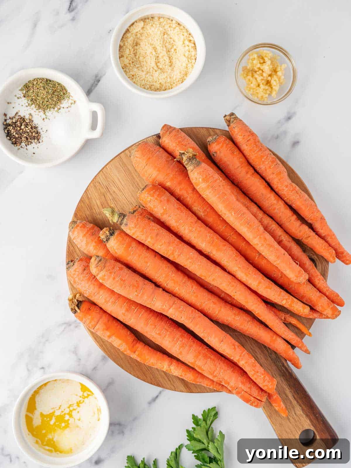 Ingredients needed for parmesan roasted glazed carrots laid out on a wooden surface, including fresh carrots, butter, garlic, Italian seasoning, Parmesan cheese, and fresh parsley.