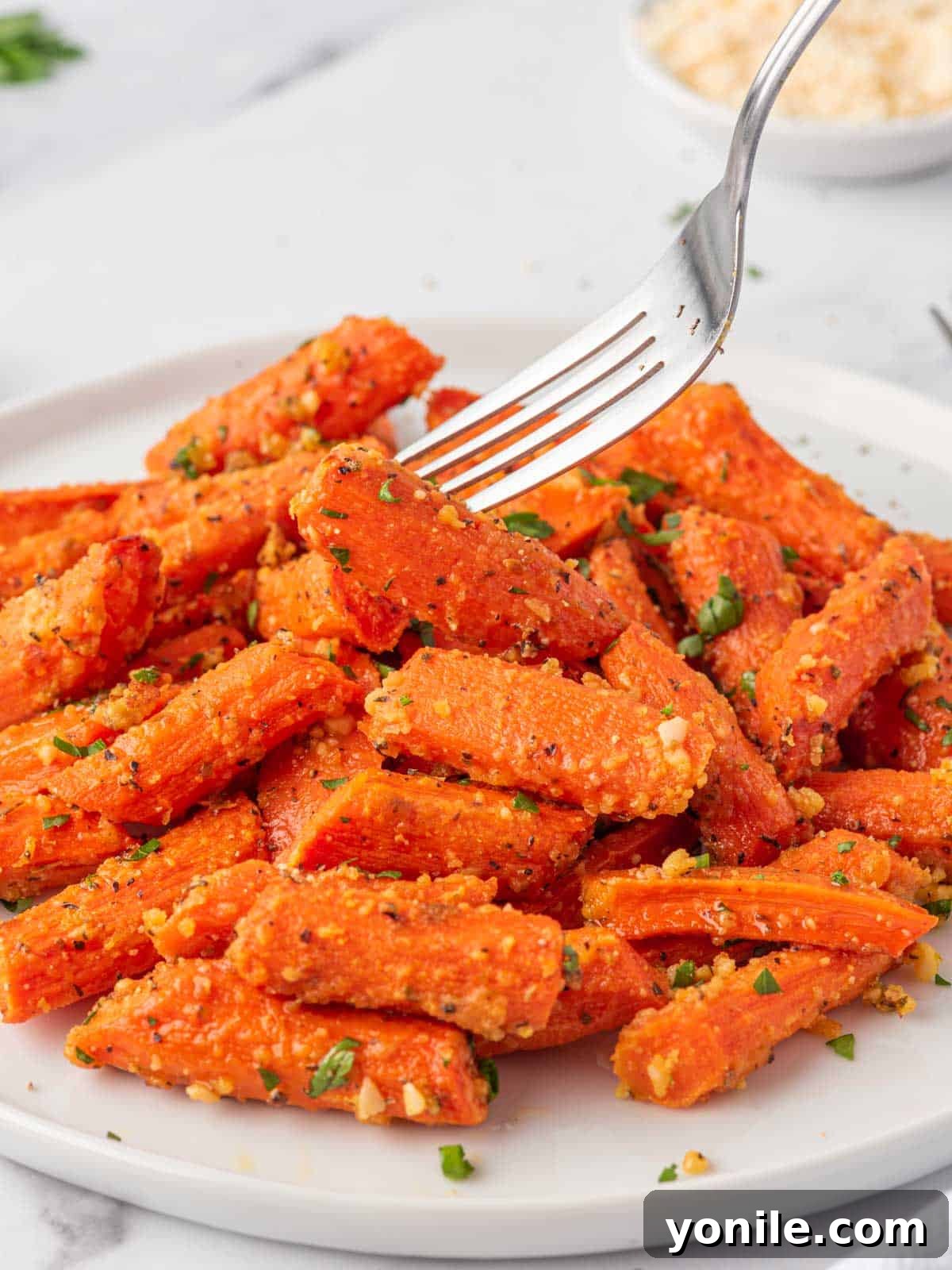 A fork picks up a perfectly oven roasted carrot, showcasing its tender texture and golden glaze.