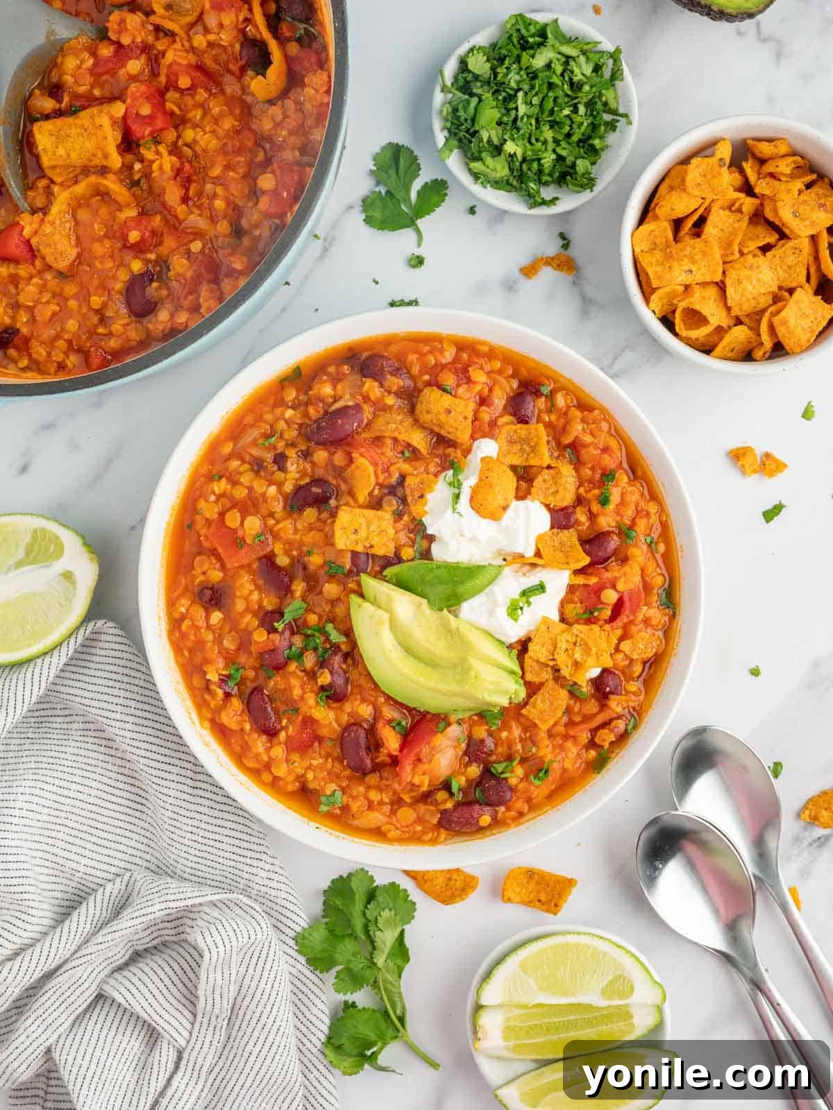 A steaming bowl of vibrant vegan chili, generously topped with fresh cilantro, creamy avocado slices, and a dollop of vegan sour cream, with lime wedges on the side, inviting a delicious and healthy meal.
