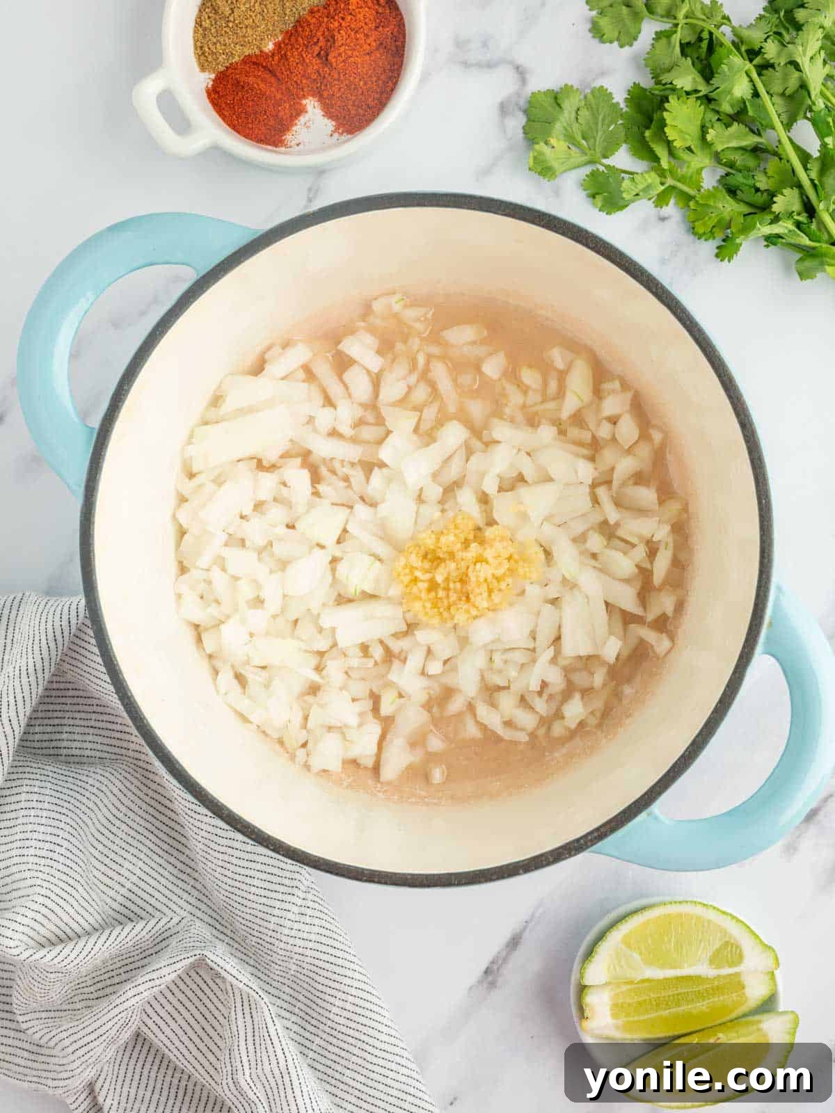 Close-up view of chopped yellow onions and minced garlic gently sizzling in olive oil within a sturdy cast iron skillet, emitting fragrant steam as they begin to soften and turn translucent, forming the aromatic base of the chili.