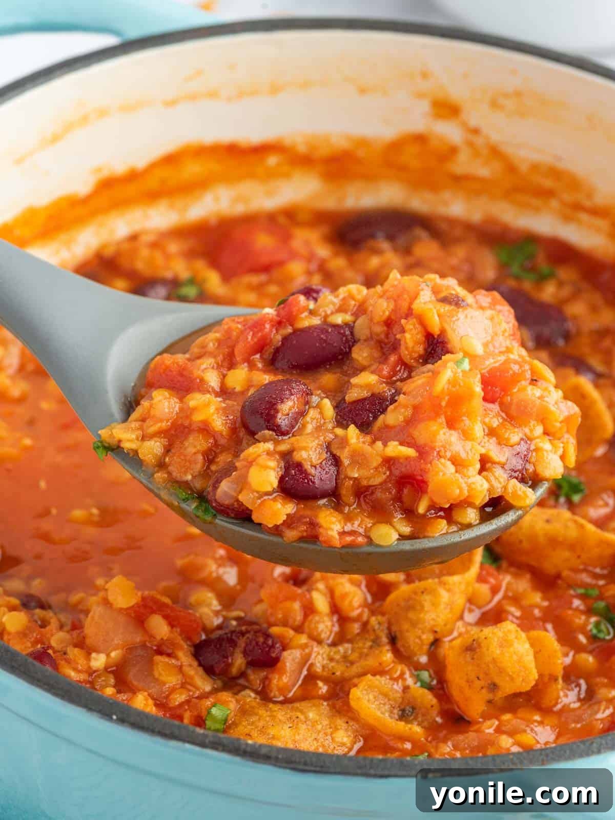 A large serving spoon elegantly scoops a generous portion of rich, textured meatless chili directly from a rustic orange Dutch oven, highlighting the thick consistency and inviting warmth of the plant-based meal, ready to be served.