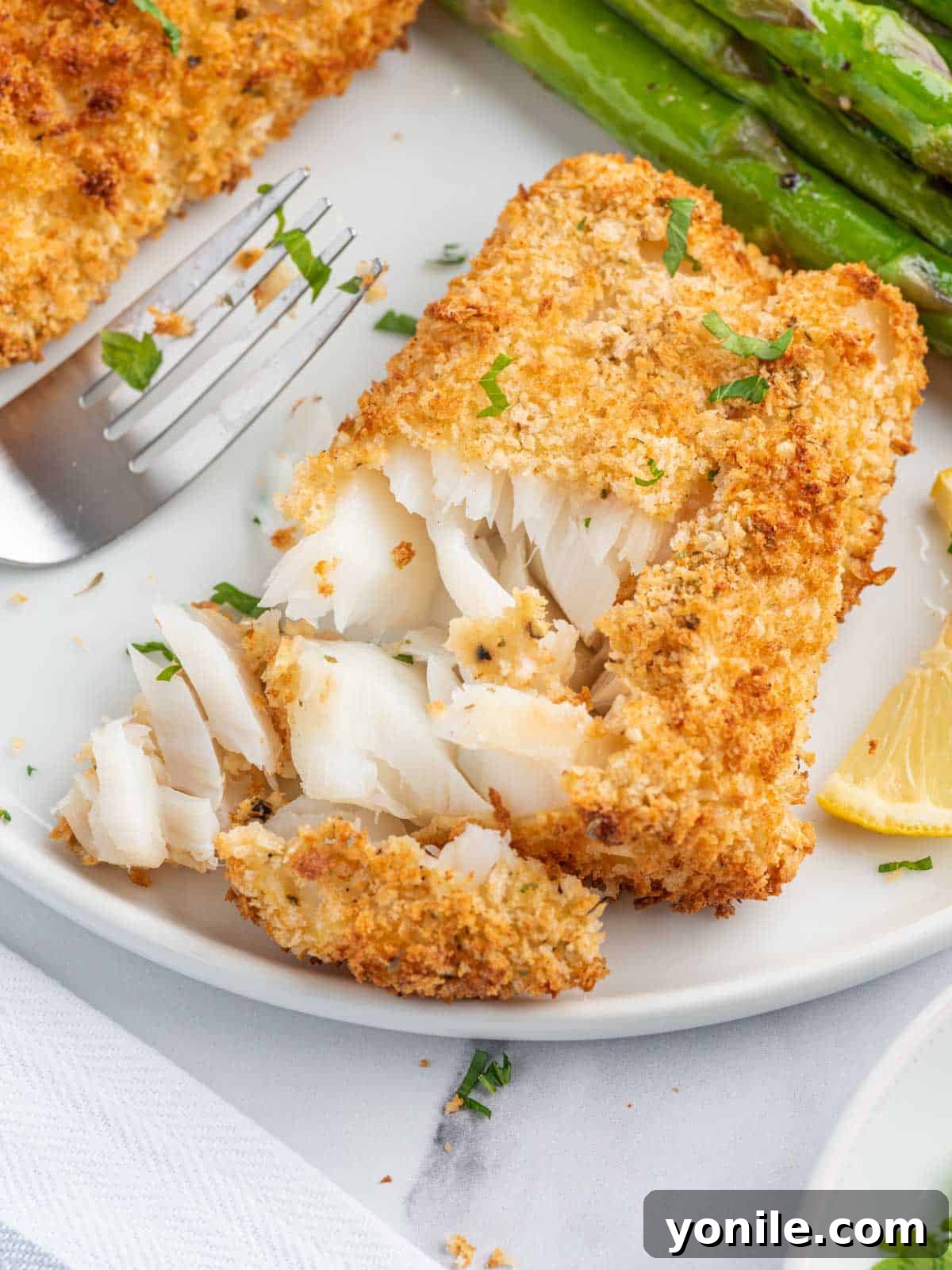 A fork flaking a piece of air-fried cod on a plate, showing its tender interior.