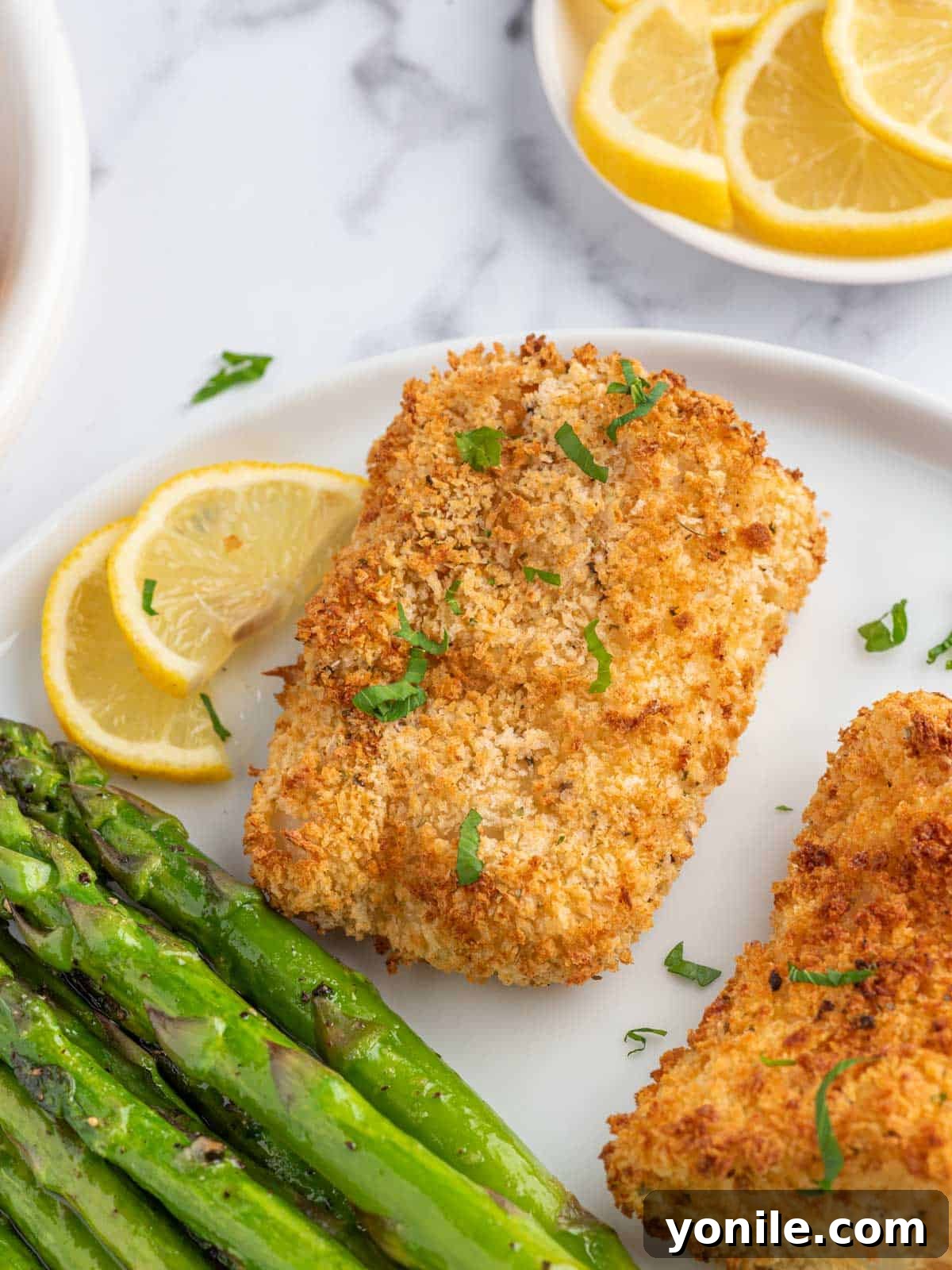 Panko crusted cod on a plate with asparagus and a lemon wedge.