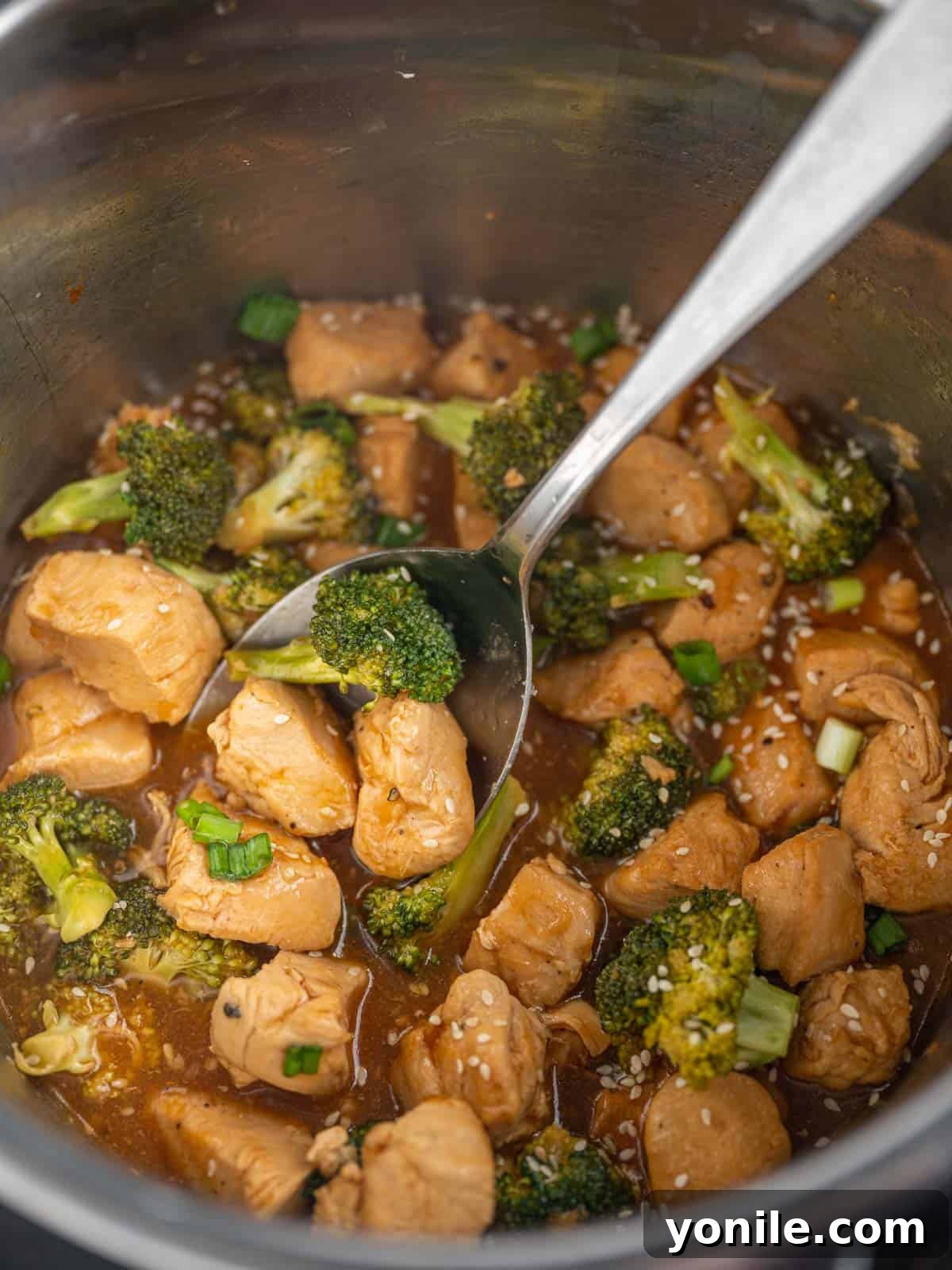 A spoon lifts a serving of chicken and broccoli from instant pot.