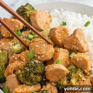 Chopsticks pick up a piece of tender chicken from a plate with rice.