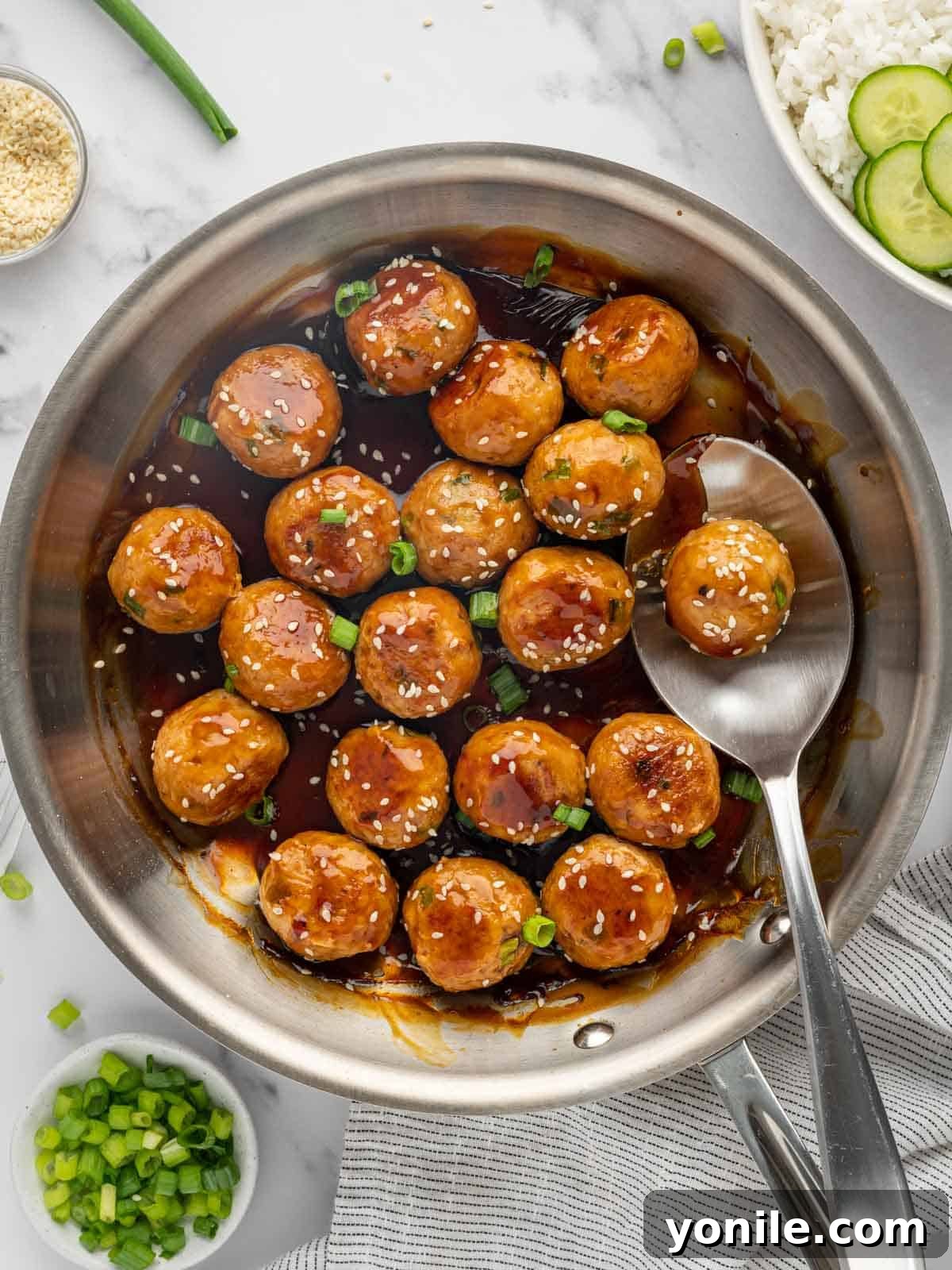Glazed Teriyaki Chicken Meatballs 2 A spoon lifts a teriyaki chicken meatball from a skillet, showing its glossy sauce.
