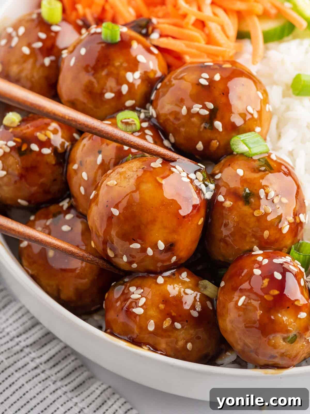 Glazed Teriyaki Chicken Meatballs 7 Chopsticks pick up a meatball coated in teriyaki sauce, ready to be eaten.