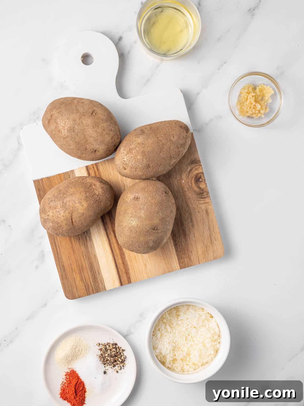 A selection of ingredients needed for making delicious air fryer potato wedges, including russet potatoes, olive oil, garlic, and parmesan cheese.