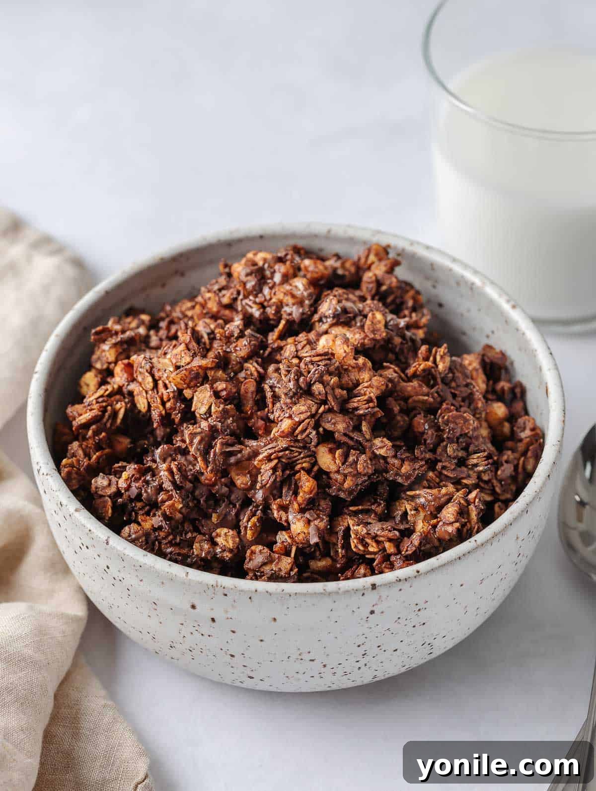 A bowl of chocolate granola with milk in a cup.