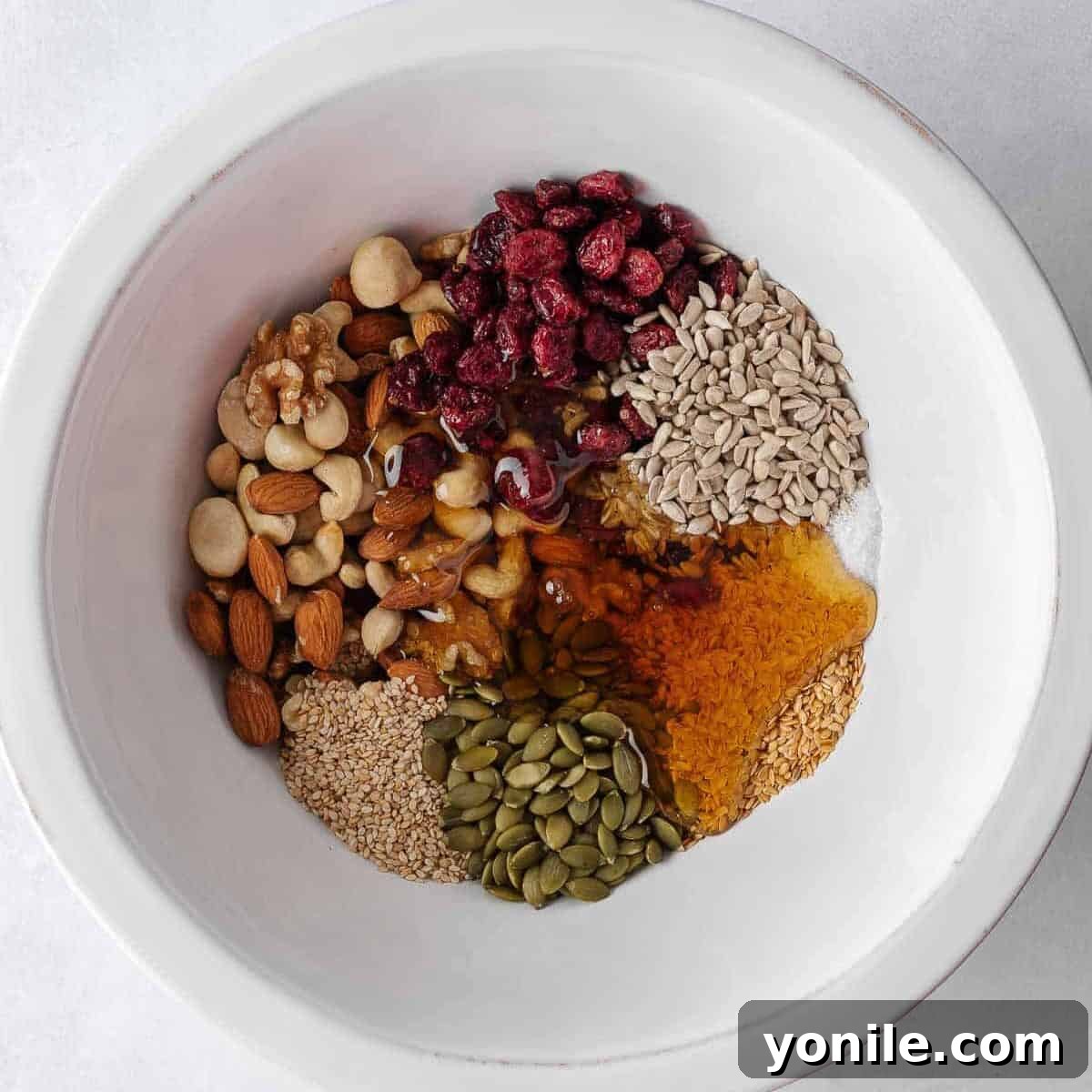 Nuts and seeds combined with honey mixture in a large mixing bowl.