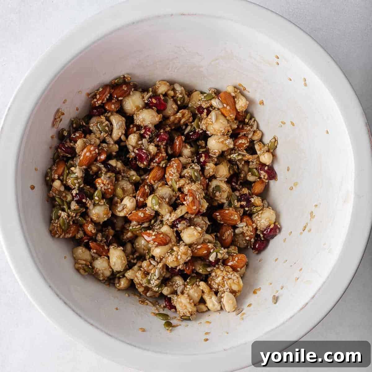 Nuts and seeds thoroughly mixed with honey and vanilla in a bowl, creating a sticky mixture.