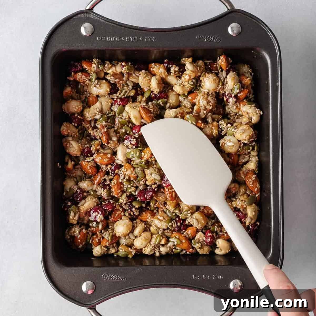 A spatula pressing the healthy nut bar mixture firmly into the parchment-lined baking pan.