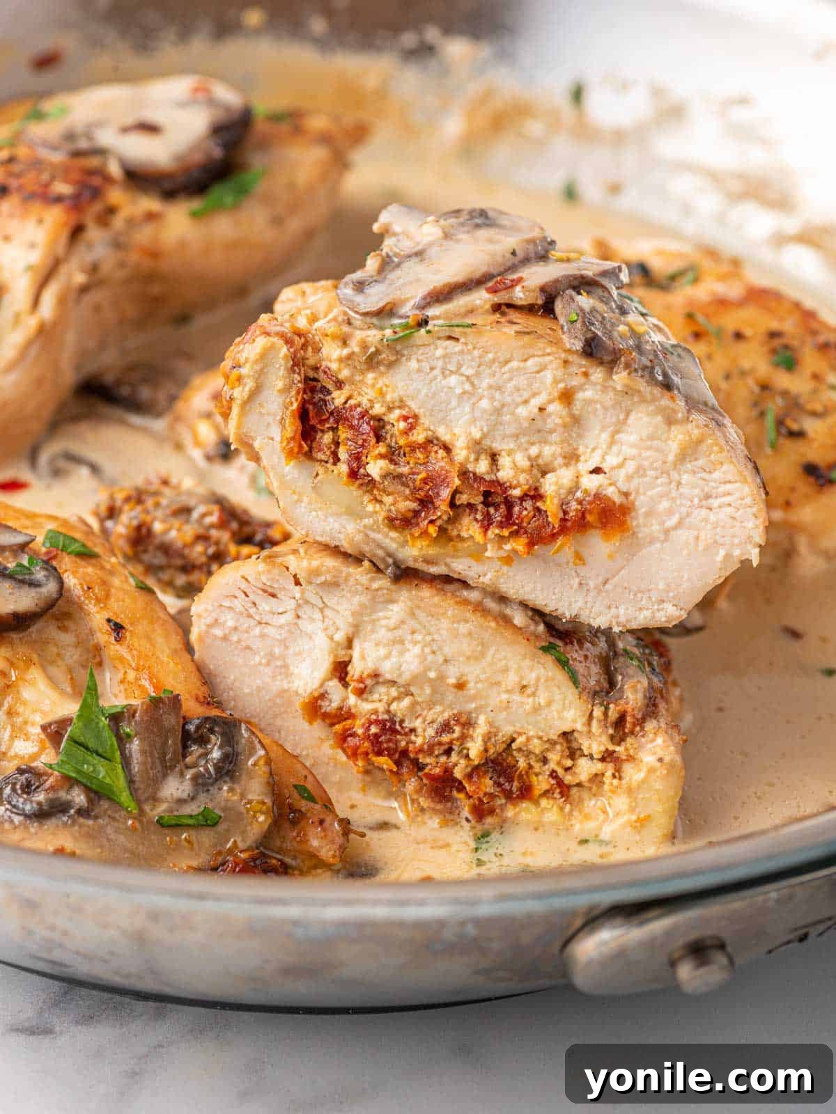 Golden-brown Stuffed Chicken Marsala, sliced in half to reveal a creamy cheese and sun-dried tomato filling, served in a cast-iron skillet with rich mushroom Marsala sauce.