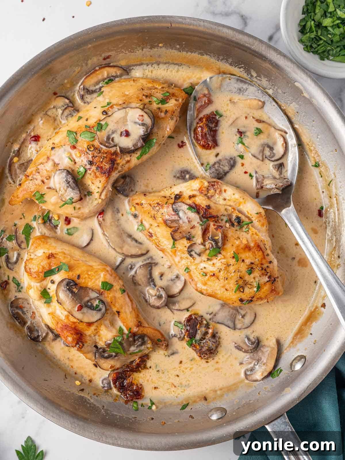 A close-up of a spoon drizzling creamy Marsala mushroom sauce over a perfectly cooked, golden Stuffed Chicken Marsala breast in a skillet.