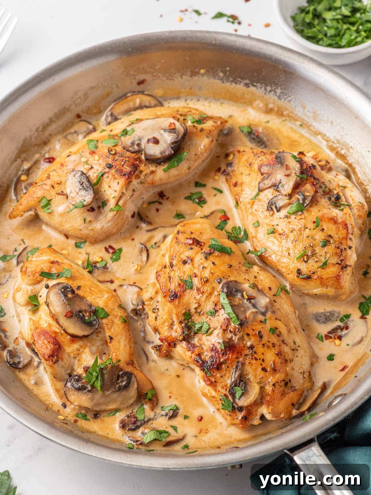 An appetizing close-up of a skillet filled with cooked Stuffed Chicken Marsala, drenched in a creamy mushroom sauce and garnished with fresh herbs, ready to serve.